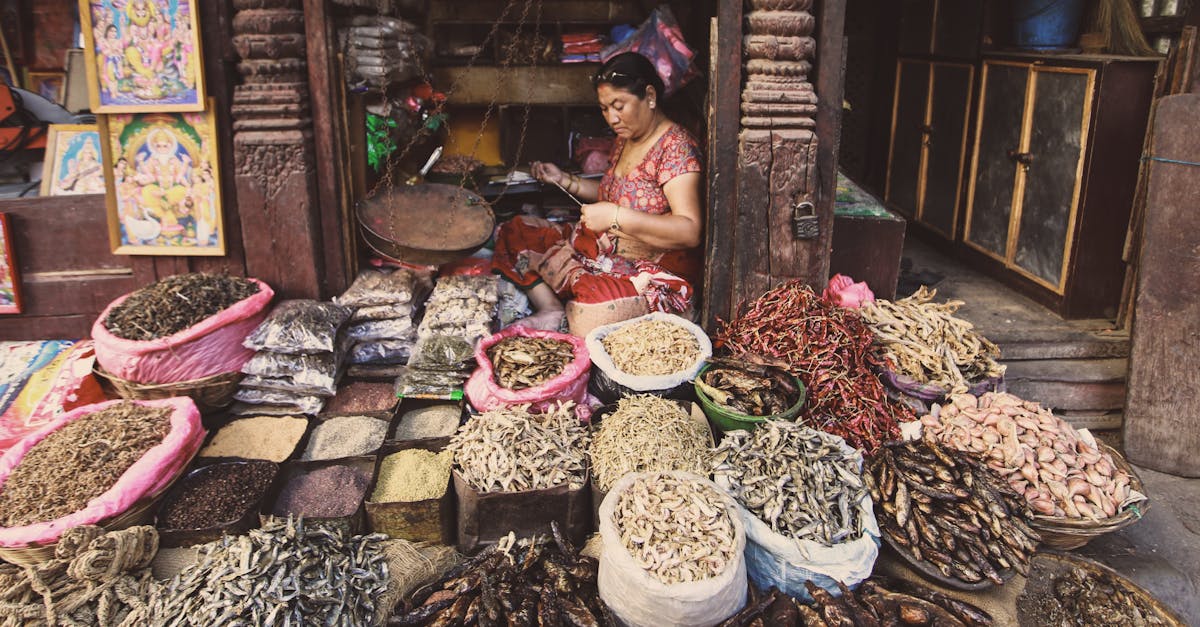 A bustling marketplace with a woman selling assorted spices, seafood, and dried goods in a traditional setting.