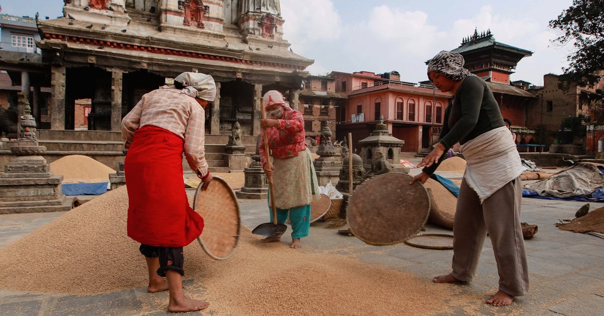 Women in Bungamati, Nepal drying grains under temple architecture on a bright day.